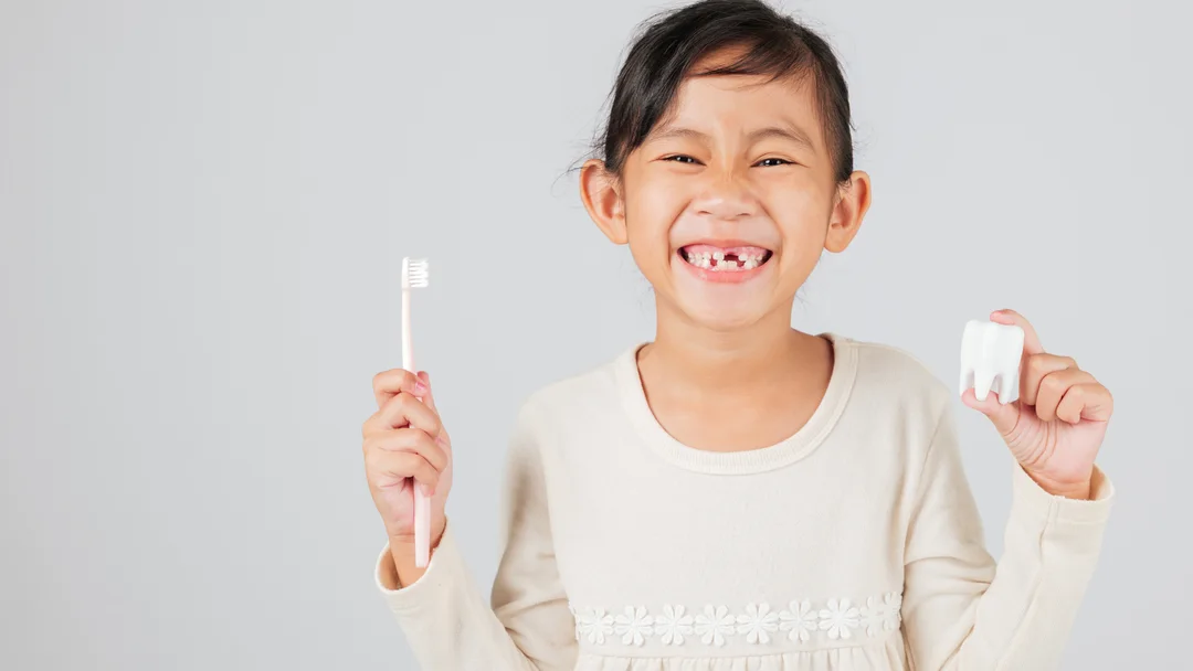 A young patient smiling at Warren Dental Associates, holding a toothbrush and a model tooth